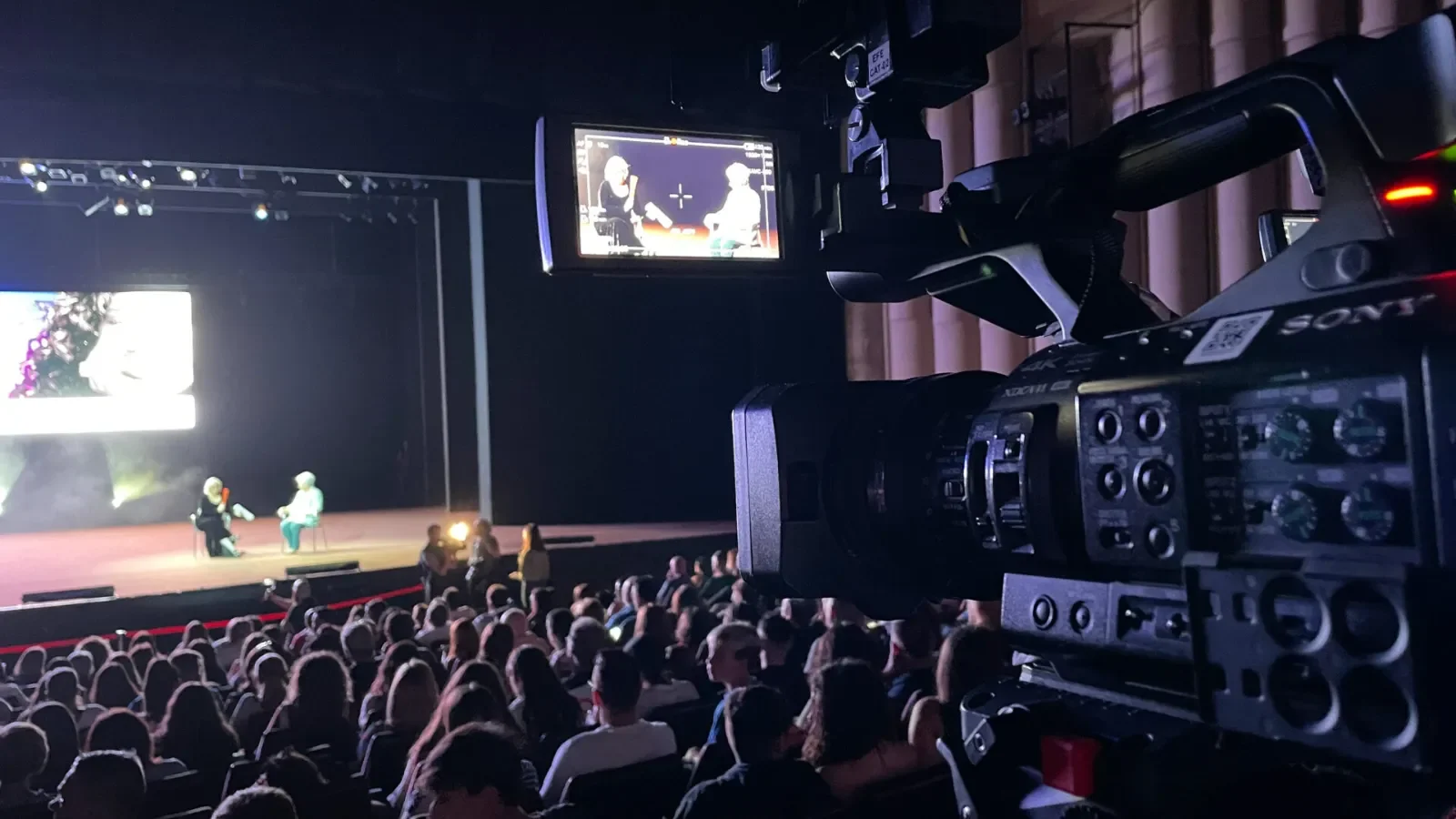 Event videographer filming a conference in a packed auditorium with a professional video camera
